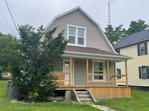 a house with a wooden porch and a tree in front of it