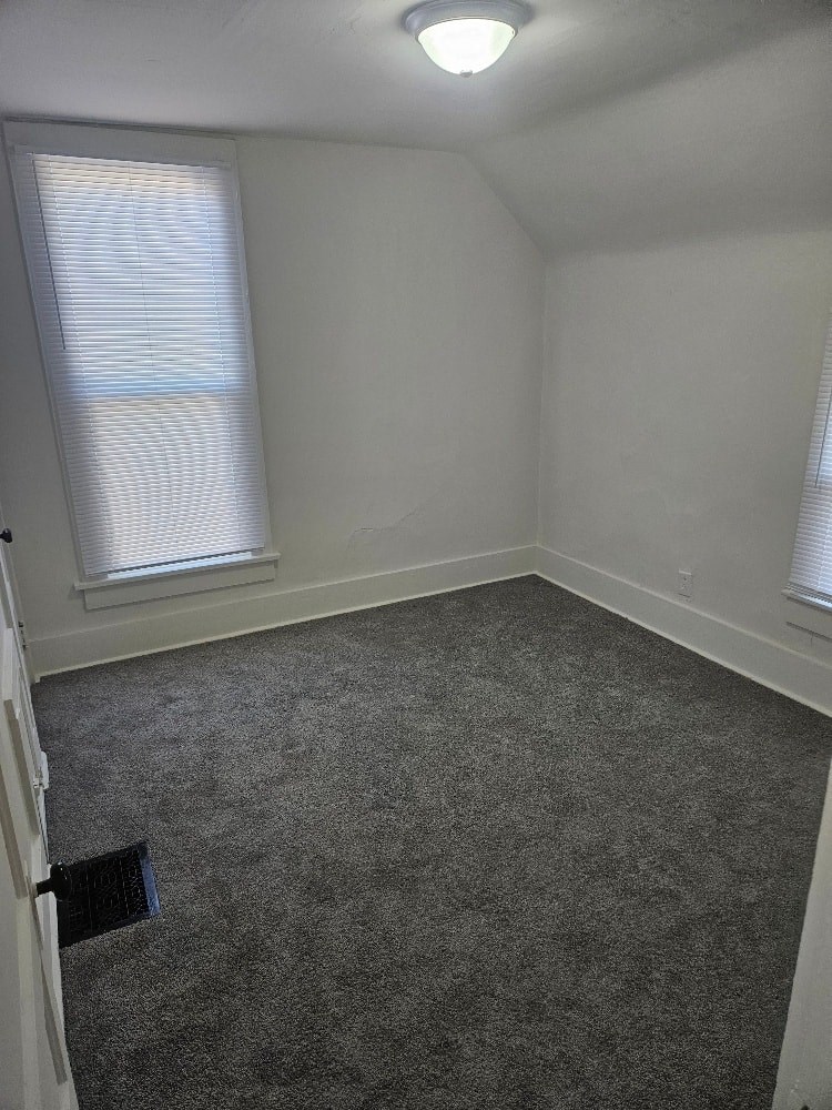A room with a carpeted floor and a window with blinds.