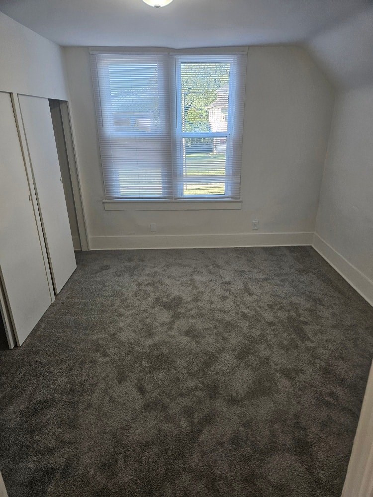 A room with a carpeted floor and a window with blinds.