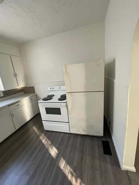 A white refrigerator stands in a kitchen with a stove and oven.