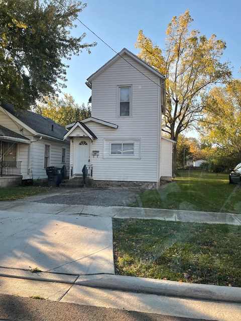 A house with a white siding and a grey roof is surrounded by a grassy lawn and trees.