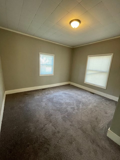 an empty room with two windows and a carpeted floor