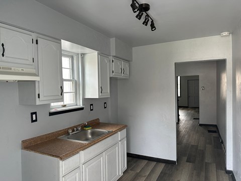 a kitchen with white cabinets and a sink   and a hallway with a door