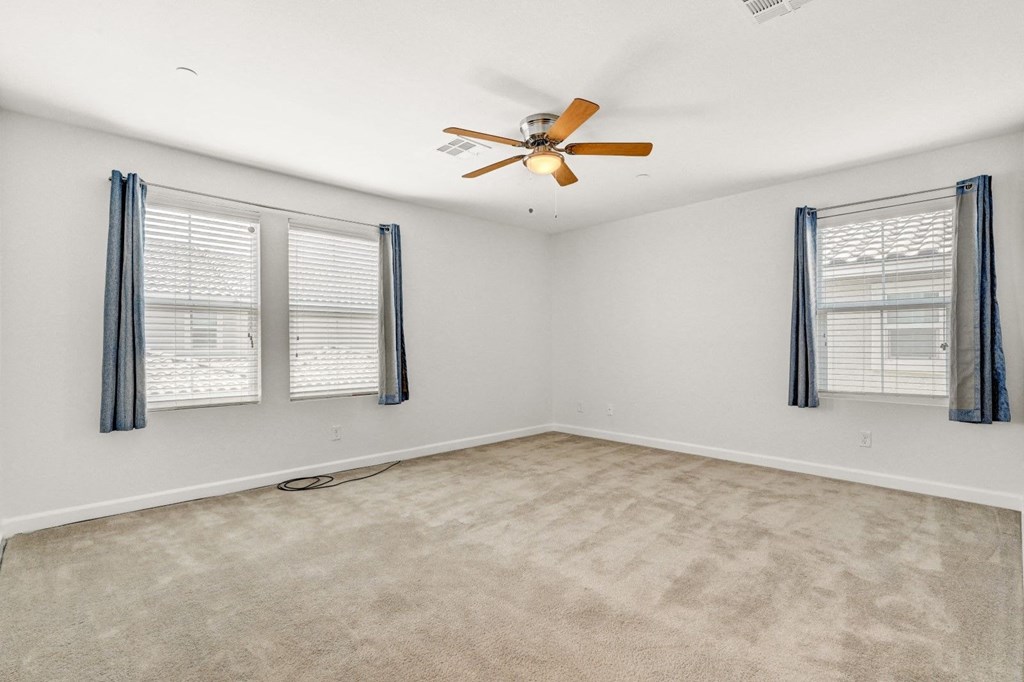 an empty living room with a ceiling fan and three windows