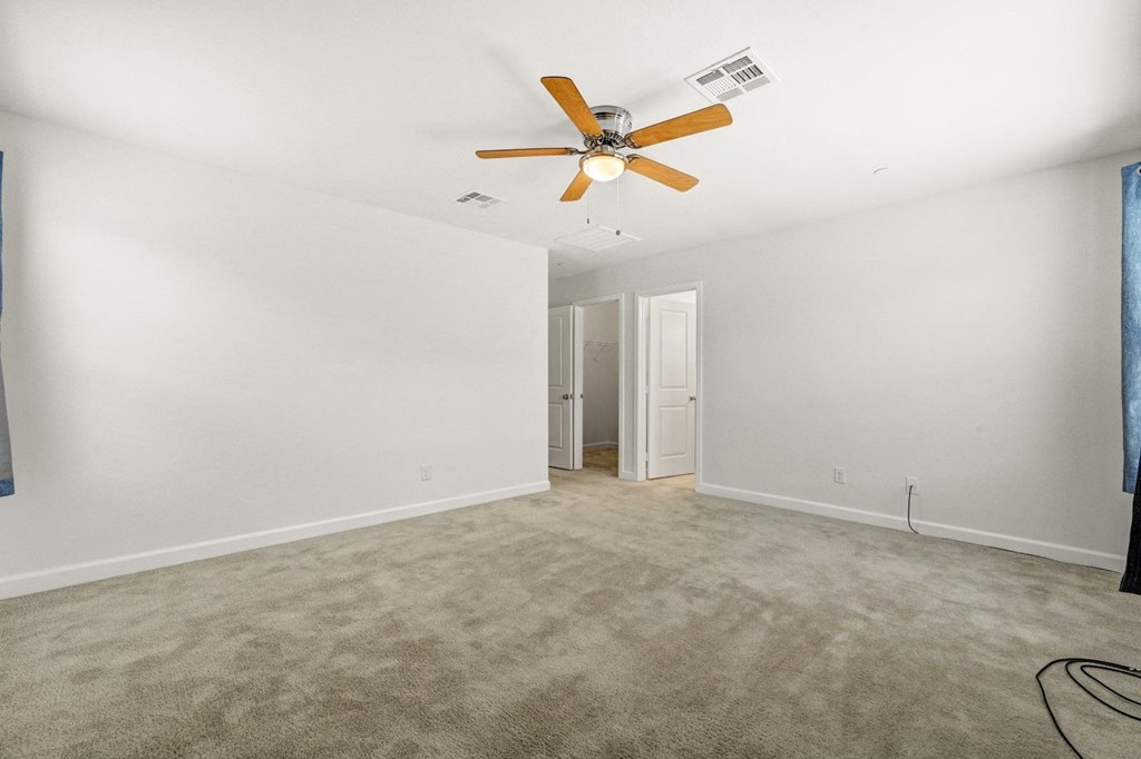 an empty living room with a ceiling fan and white walls