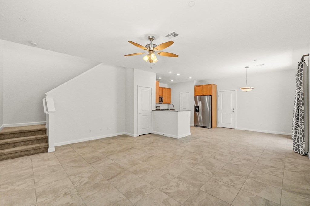 an empty living room with a ceiling fan and a kitchen