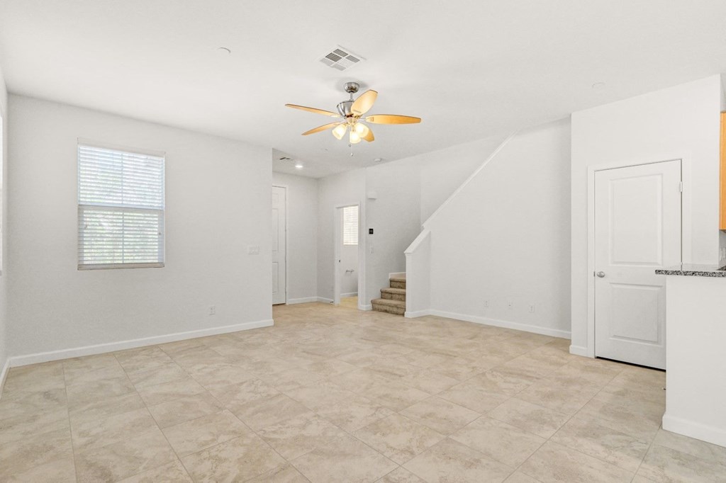 an empty living room with a ceiling fan and a staircase