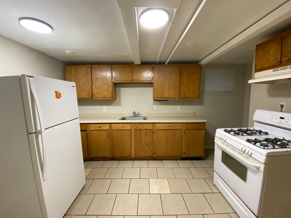 A kitchen with a white refrigerator, white stove, and wooden cabinets.