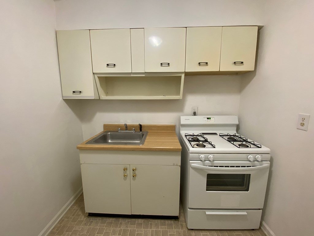 A small kitchen with a stove, sink, and cabinets.