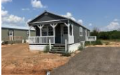 A small house with a porch is surrounded by a dirt field.