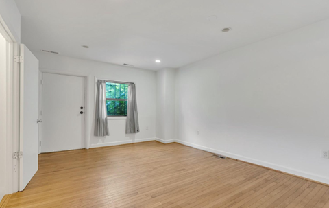 a living room with white walls and a window and wooden floors