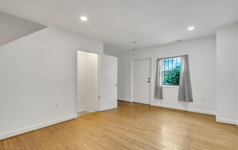 a living room with white walls and a window and wooden floors