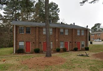 the front of a brick house with red doors and a tree