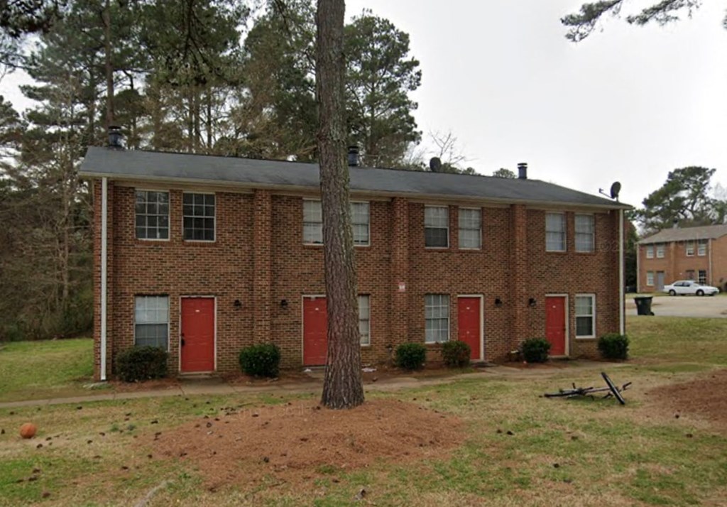 the front of a brick house with red doors and a tree