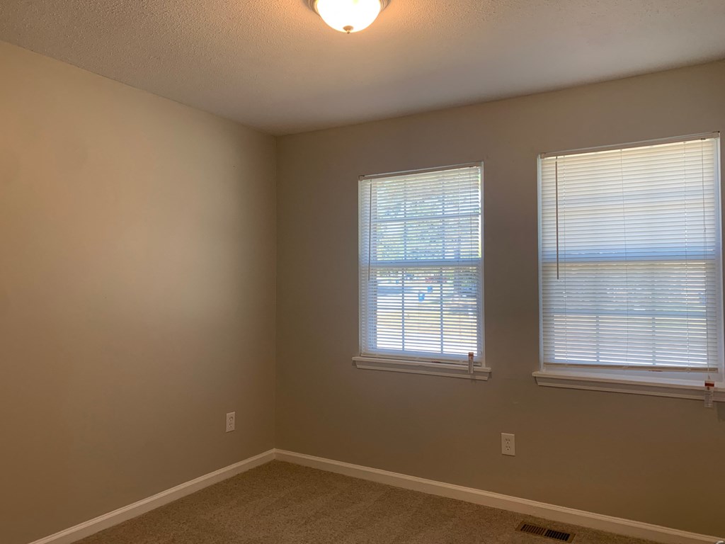 a bedroom with two windows and a carpeted floor