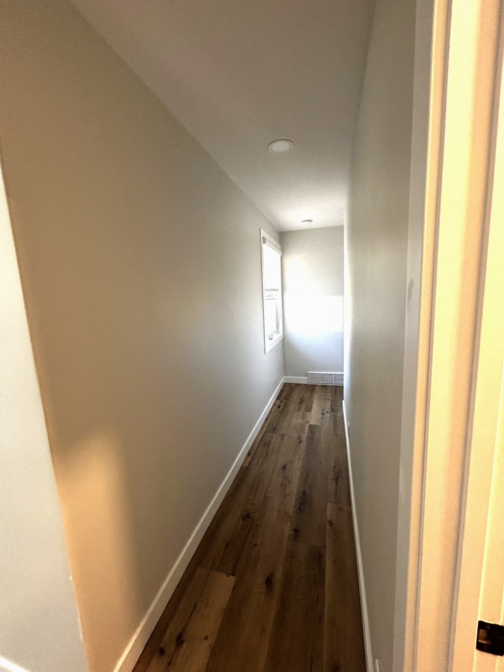 a hallway with white walls and wooden floors and a window