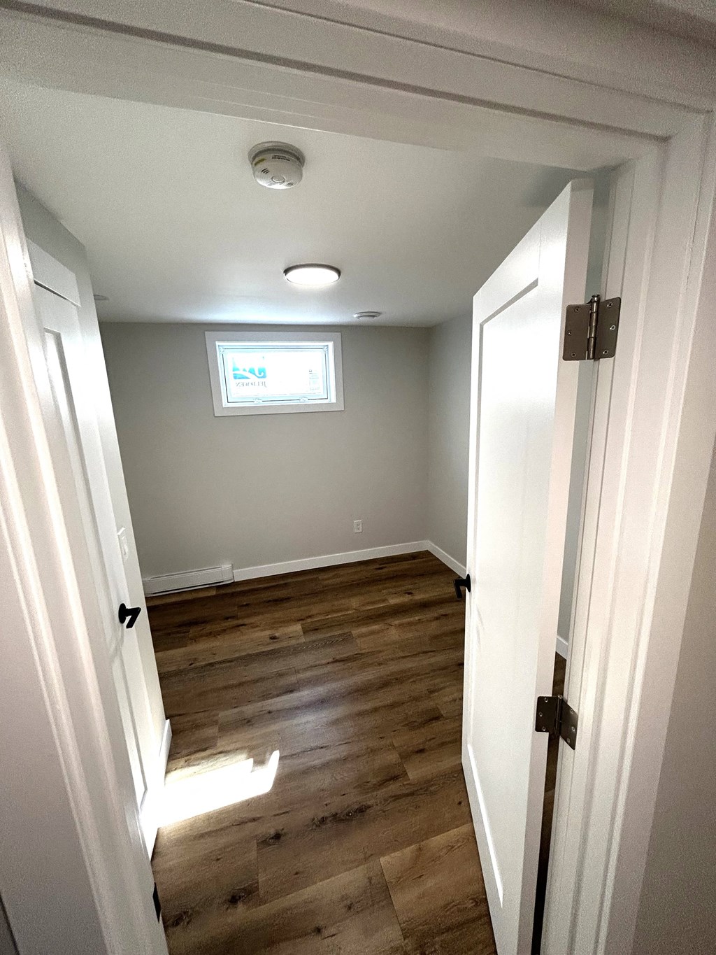 a small room with wooden floors and a window and a white door