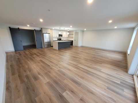 A spacious room with wooden flooring and a kitchen area in the background.