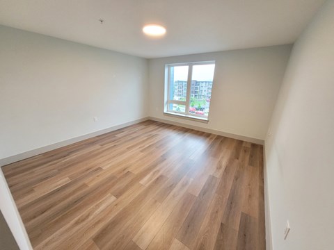 A room with wooden flooring and a window overlooking a building.