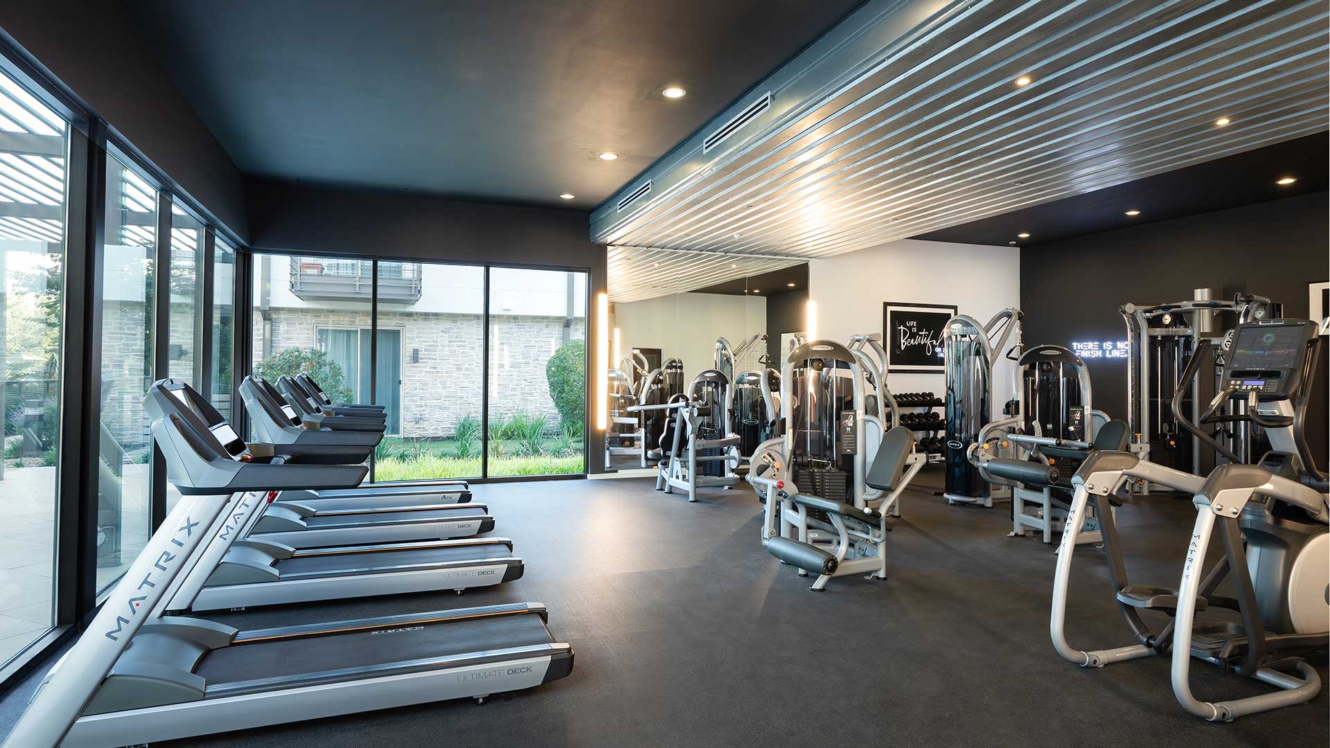 A gym room with tread machines, weight machines, and large windows.