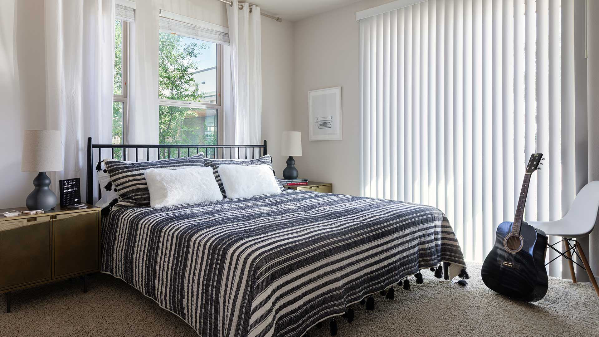 A bedroom with striped bedding and a guitar.