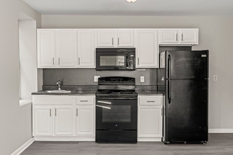 A black refrigerator stands in a kitchen with white cabinets and appliances.