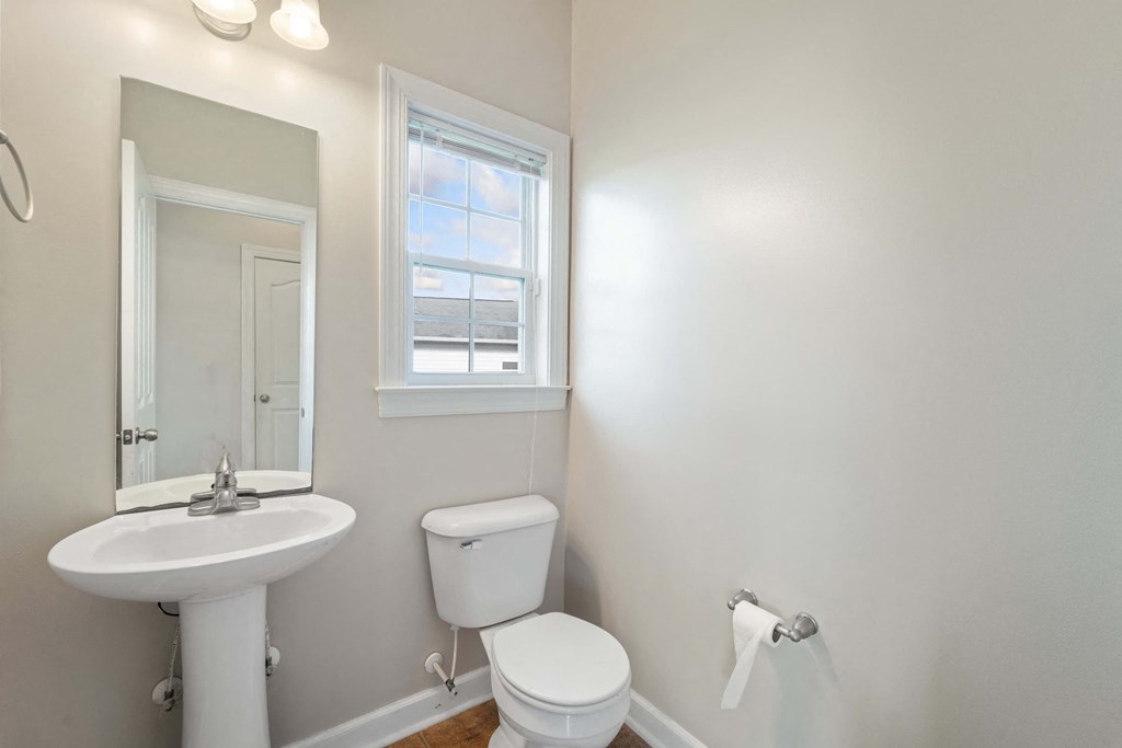 a bathroom with a toilet sink and mirror and a window
