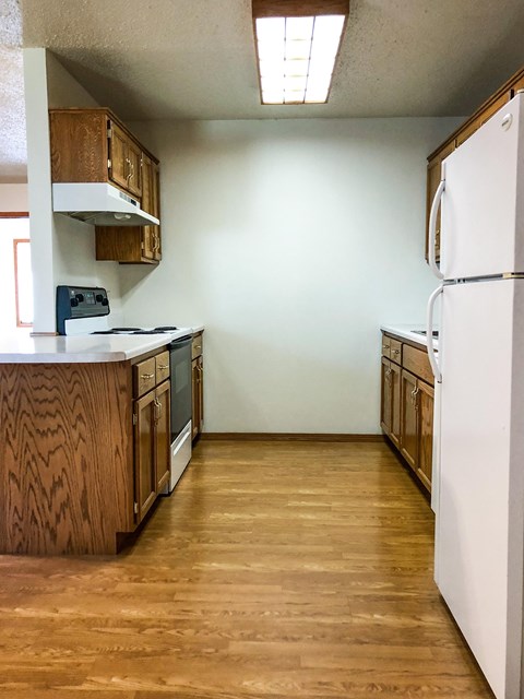 an empty kitchen with white appliances and wooden cabinets