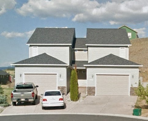 Two cars are parked in front of a white house.