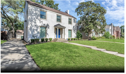 A white house with a blue door and windows is surrounded by a green lawn.