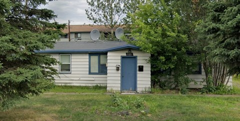 A small house with a blue door and windows surrounded by trees.