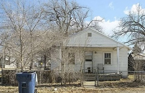 A white house with a blue trash can in front of it.