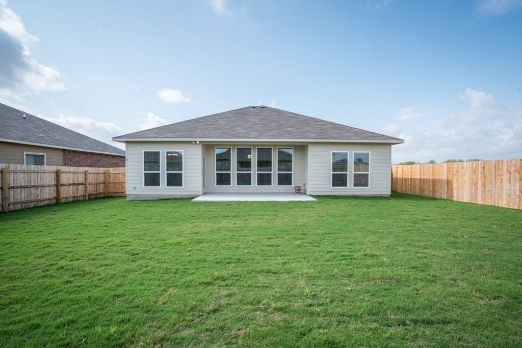 A house with a white exterior and a grey roof is surrounded by a wooden fence.