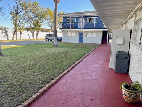 A red pathway leads to a white building with a blue balcony.