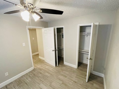 A room with a ceiling fan and three open closets.