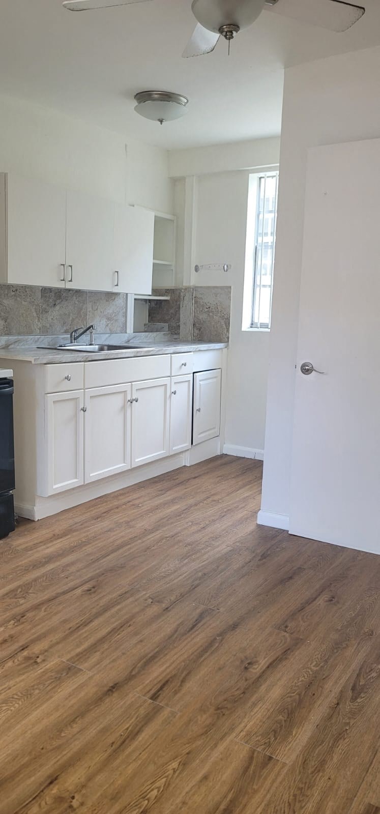 an empty kitchen with white cabinets and a wooden floor