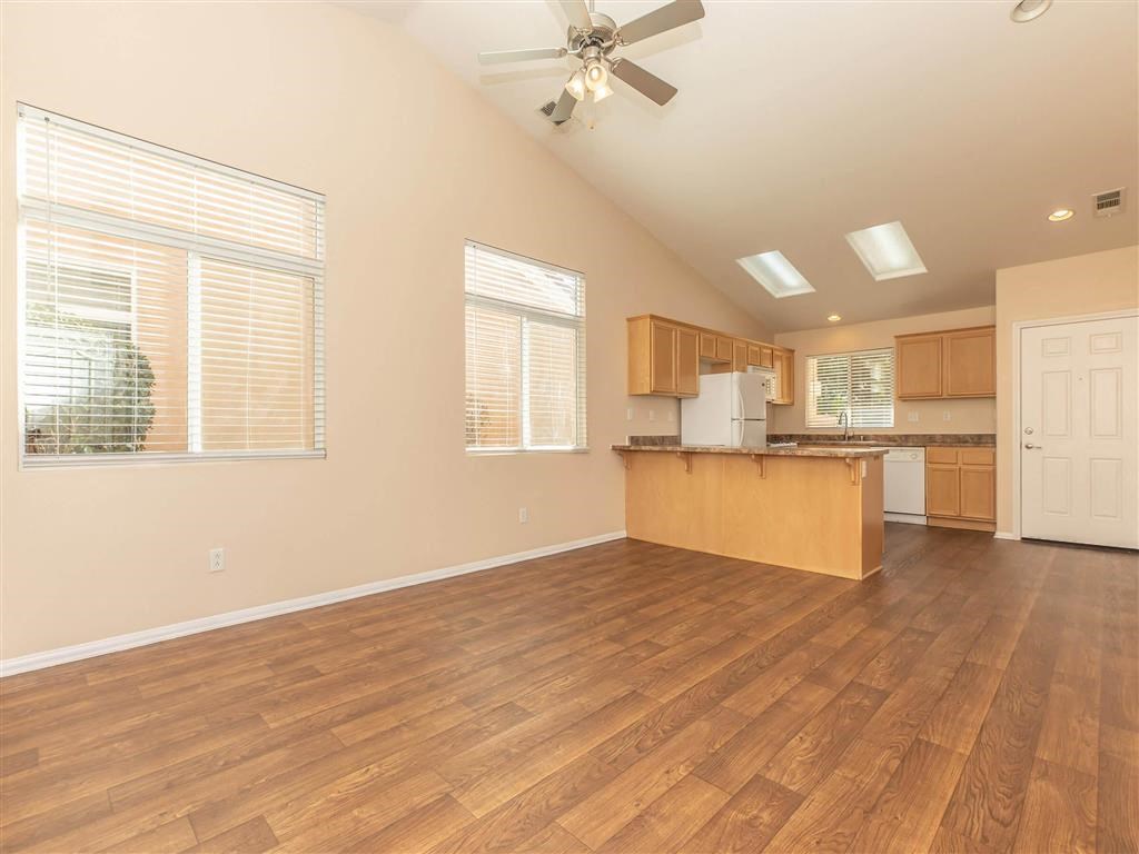 an empty living room with a kitchen and a ceiling fan