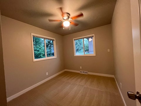 A room with a ceiling fan and two windows.