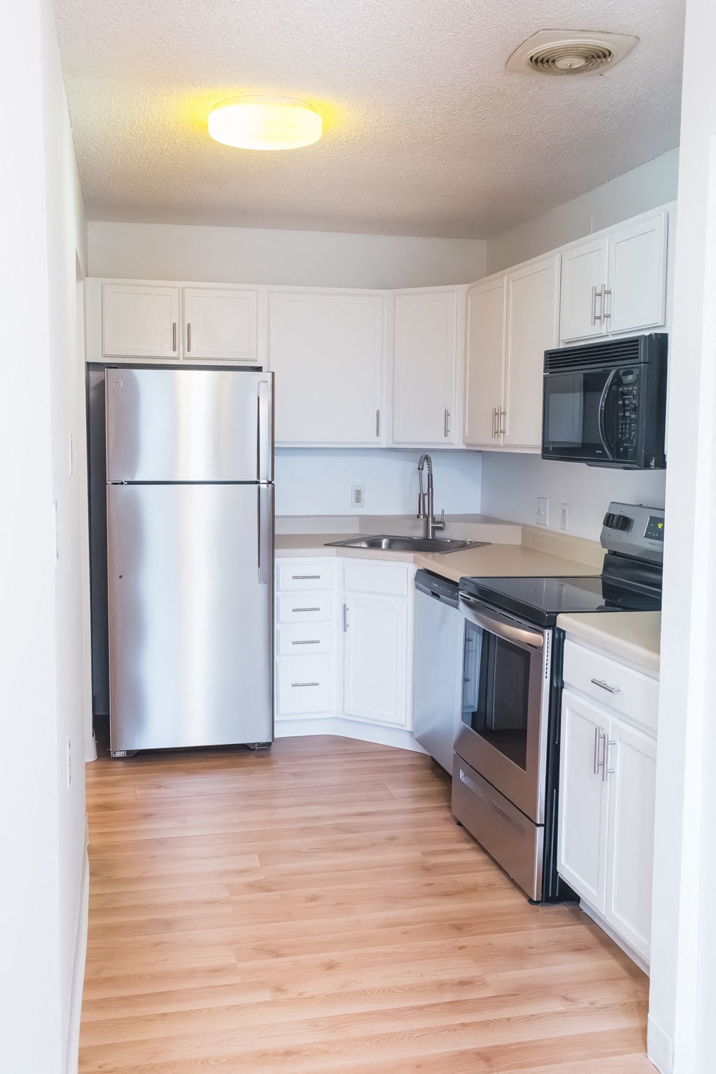 an empty kitchen with stainless steel appliances and white cabinets