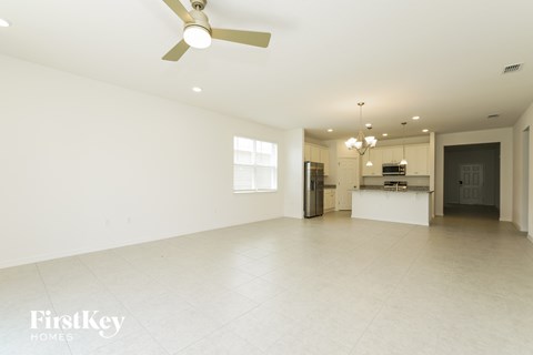A spacious, empty room with a ceiling fan and a kitchen area in the background.