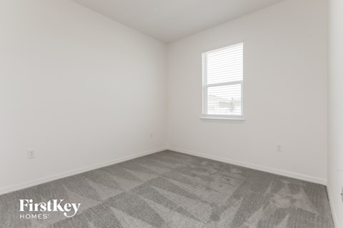 a bedroom with white walls and a window and gray carpet