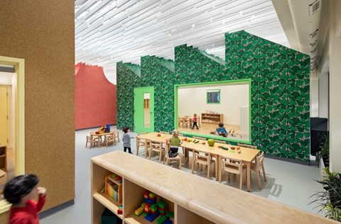 A group of children playing in a room with a green wallpaper.