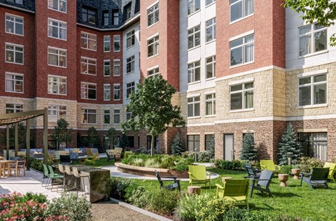 a courtyard with green chairs and a garden in front of an apartment building