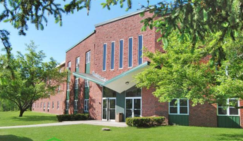 a large brick building with a green lawn and trees