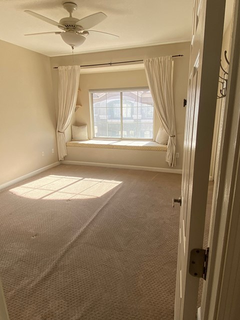 an empty living room with a window and a ceiling fan