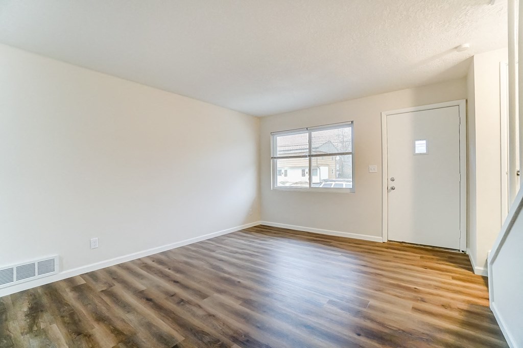 an empty living room with wood flooring and a window
