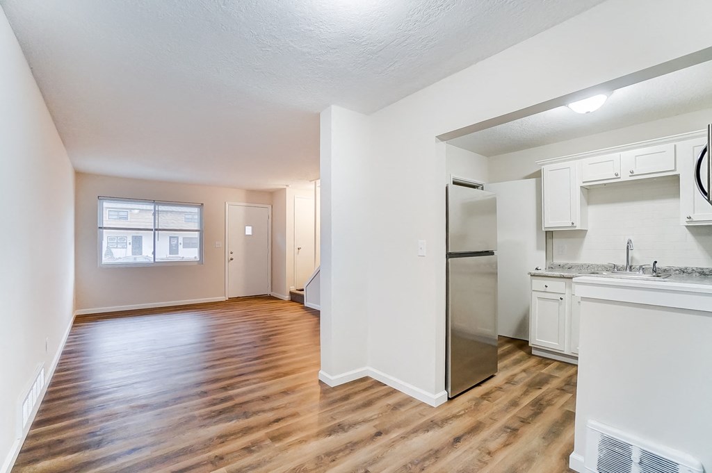 an empty living room and kitchen with wood flooring and a refrigerator