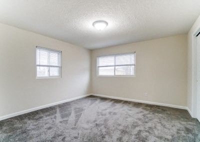an empty room with a carpeted floor and two windows