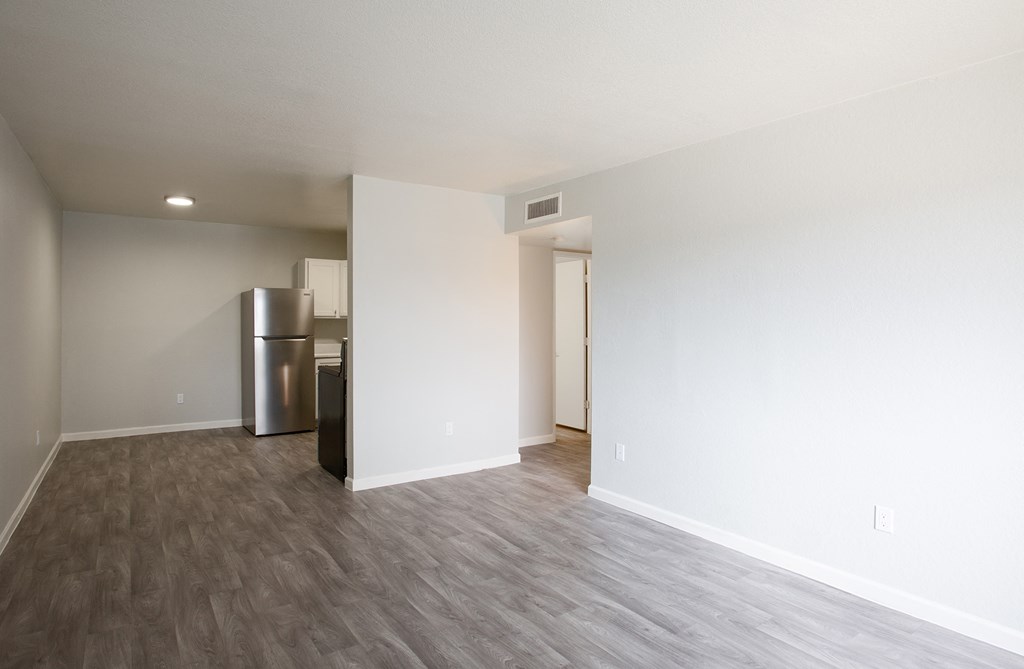 an empty living room with white walls and a stainless steel refrigerator