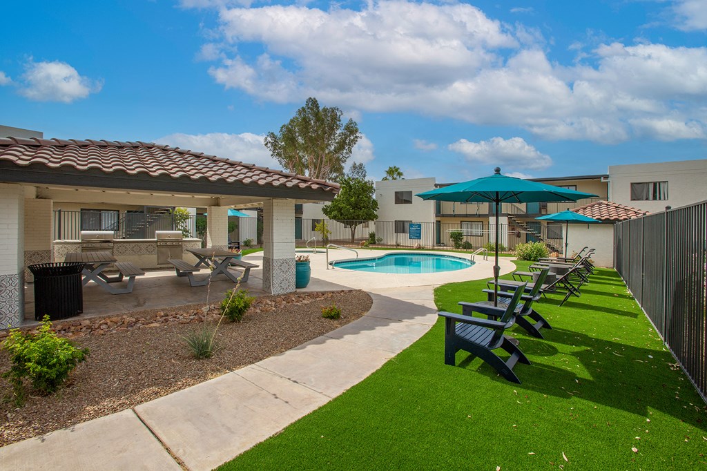 a backyard with a pool and patio with benches and umbrellas